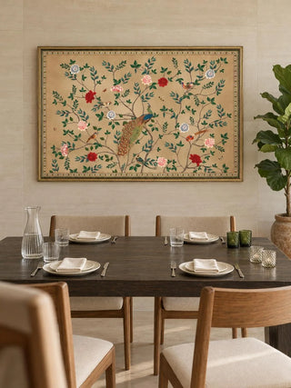 The Pakhi wall art in a slim gilt frame above a dark dining table with oak chairs, green glass votives and a fiddle-leaf plant.