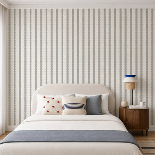 The Pebble Stripe cream grey wallpaper installed behind a cream upholstered bed with a rattan table lamp and wood nightstand view-bedroom