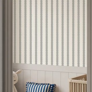 The Pebble Stripe cream grey wallpaper installed above wainscoting in a nursery beside a wood crib and plush lamb toy view-nursery