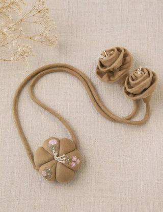 A flat lay view of the Petal Knot tie back showcasing the full layout of the puff flower emblem, padded loop cord, and rose drops.