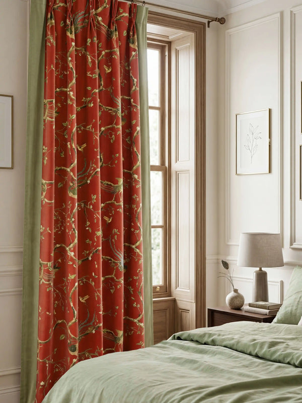 Phoenix Chinoiserie curtains framing a window in a modern bedroom with neutral walls and sage green bedding.