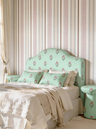 A luxury bedroom featuring a custom headboard and matching cushions upholstered in Phool Bagh mint green floral fabric against a striped wallpaper.