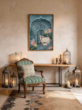 Pichwai cow and calf mural wall art in teal mist, framed in light oak above a slim console with candles, birdcage lanterns and a green striped armchair in an entryway.