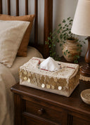 The Pitara tissue case in Oatmeal, view-bedside beside a potted plant and table lamp.