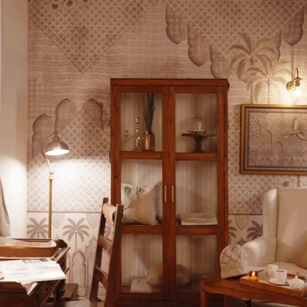 Alhambra's Whisper wallpaper with lattice arches and palm trees, behind a glass cabinet, armchair and tea table in a sitting room
