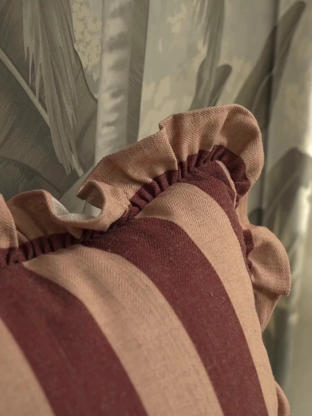 Cinnamon Ruffle cushion cover in maroon and peach stripes with a gathered ruffle edge, up close and on a sofa beside white flowers