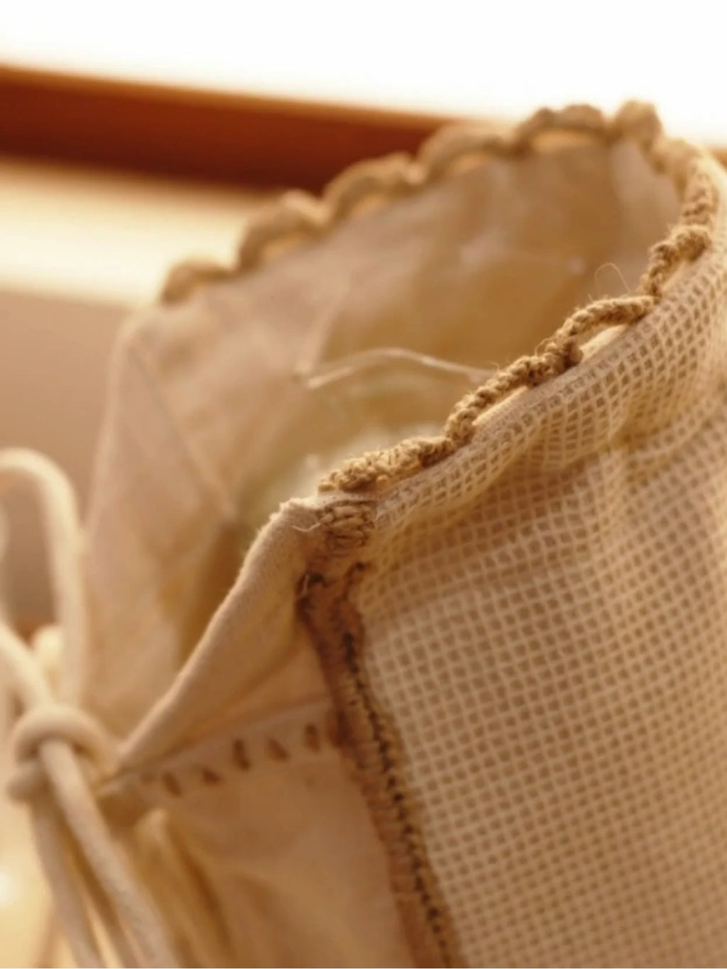 Deep Lore jug cover in ivory mesh with a scalloped edge and drawstring tie, covering a glass jug on a wooden tray beside tumblers
