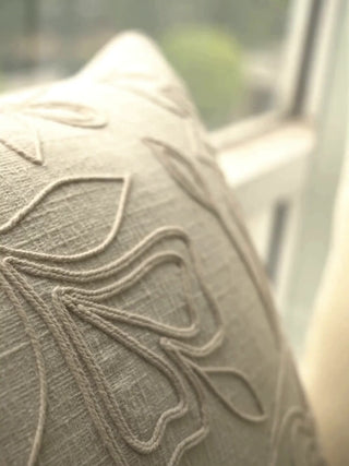 Eden cushion cover in ivory linen with raised tonal leaf and vine outlines, up close and on a window seat with plants and flowers