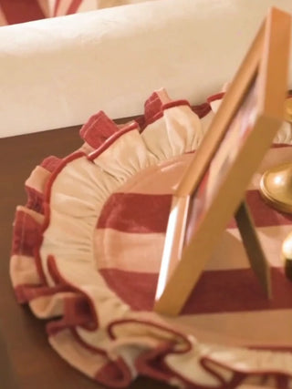 Florentine Ruffle round table mats in maroon and cream stripes with gathered ruffles, under a photo frame and brass candlesticks