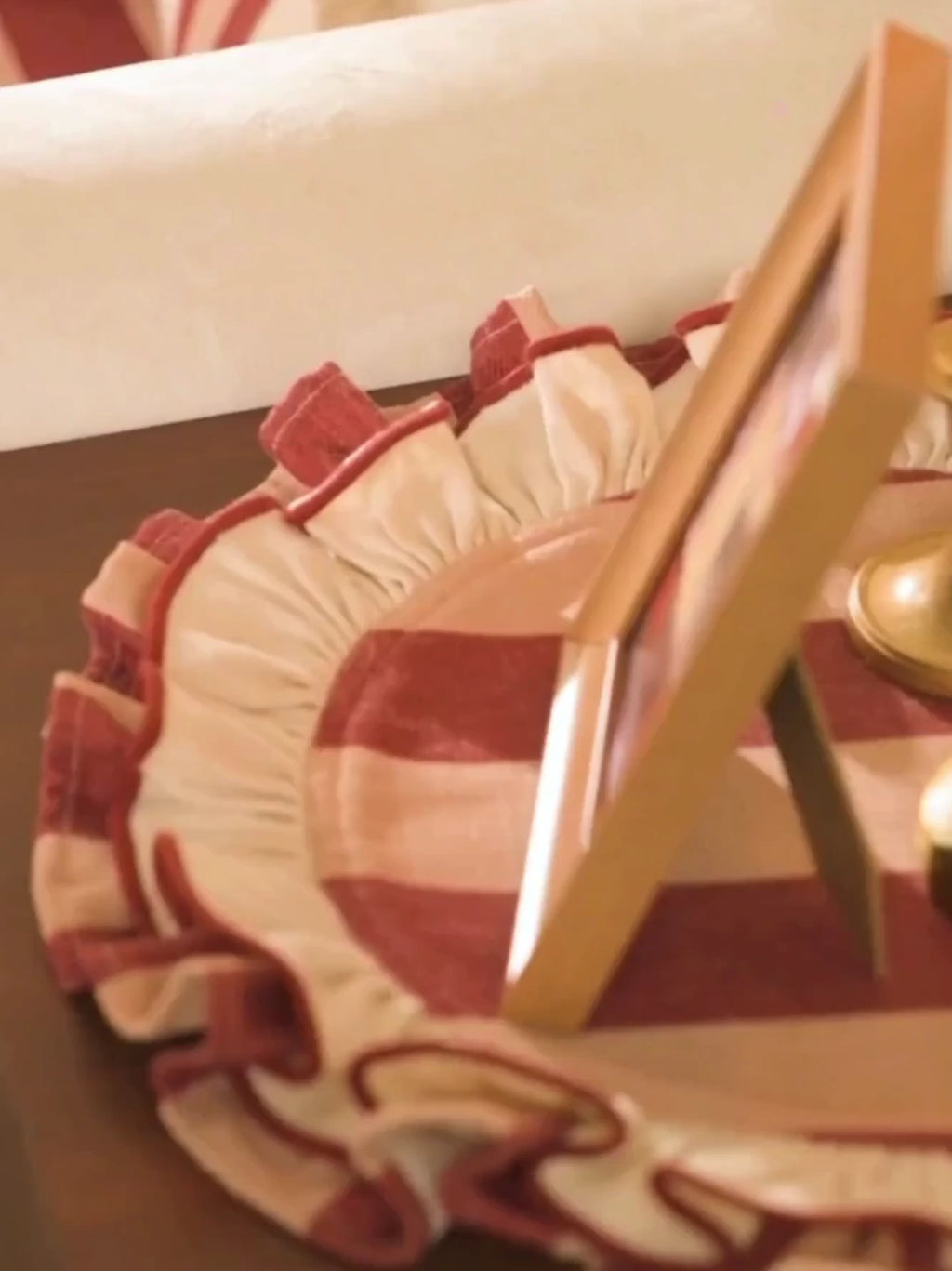 Florentine Ruffle round table mats in maroon and cream stripes with gathered ruffles, under a photo frame and brass candlesticks