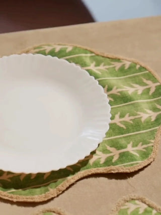 Garden Gala table mats in sage green with cream leaf sprigs and a scalloped edge, set with white plates beside glowing candles
