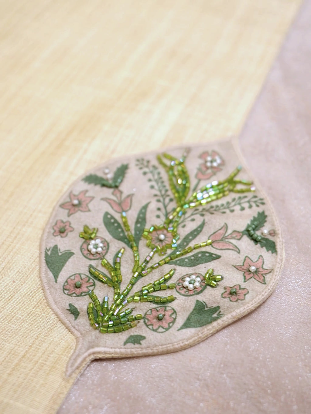 Gulnaz table runner in ivory with beaded floral leaf medallions and a tassel fringe, laid down a dining table set with a plate