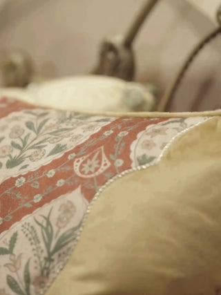 Heritage Tie cushion cover with a rust floral panel, ivory leaf medallions and a tasselled tie over a tan ground, shown up close