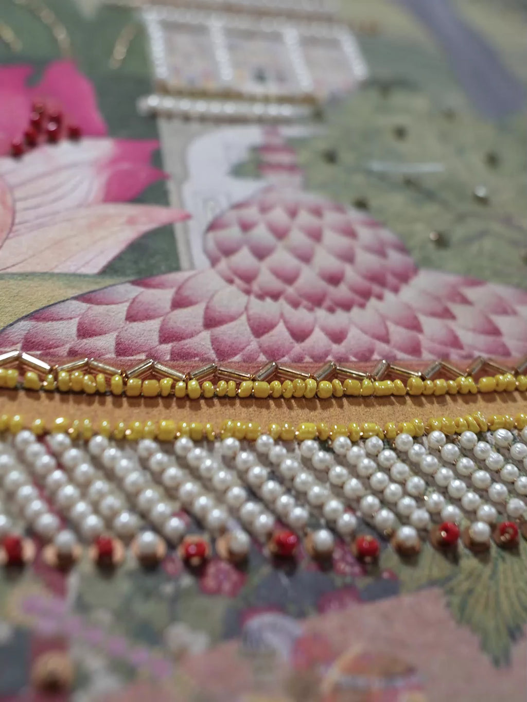 Close view of Mewar embroidered wall art: pearl and bead work on a pink lotus, green trees and a white palace in a royal garden scene