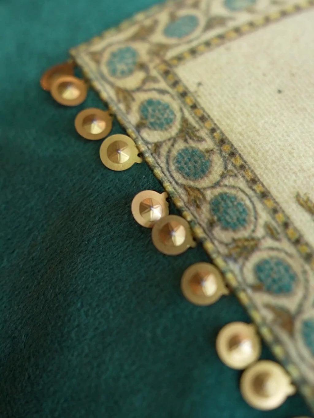 Close-up video of the Nayab velvet cushion cover in Teal, moving along the gold sequin trim and the printed flowering-shrub panels on ivory
