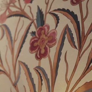 Petals of Persia wallpaper in cream with crimson flowers and sweeping leaves, shown up close by a brass lamp and behind a bed