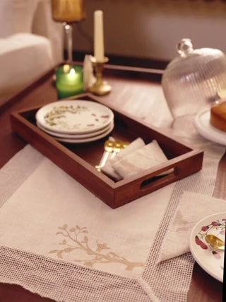 Rooted Grace table mats with an embroidered branch and open mesh border, set on a wooden coffee table with a tray, plates and fruit