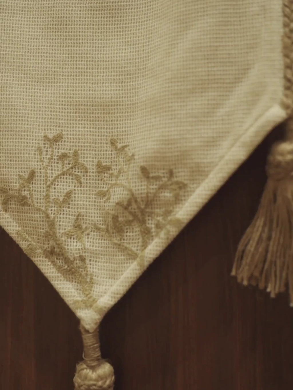 Rooted Grace table runner in ivory with a gold embroidered sprig and jute tassels, draped over the end of a dark wood console