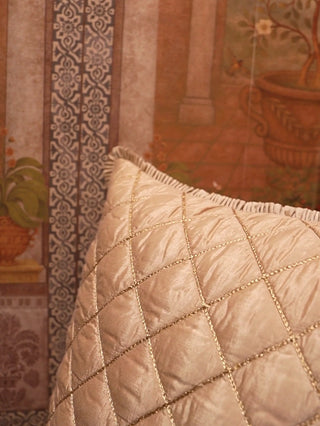 Rukhsar quilted silk cushion cover in gold with diamond quilting and a ruffled edge, shown up close against a painted wall