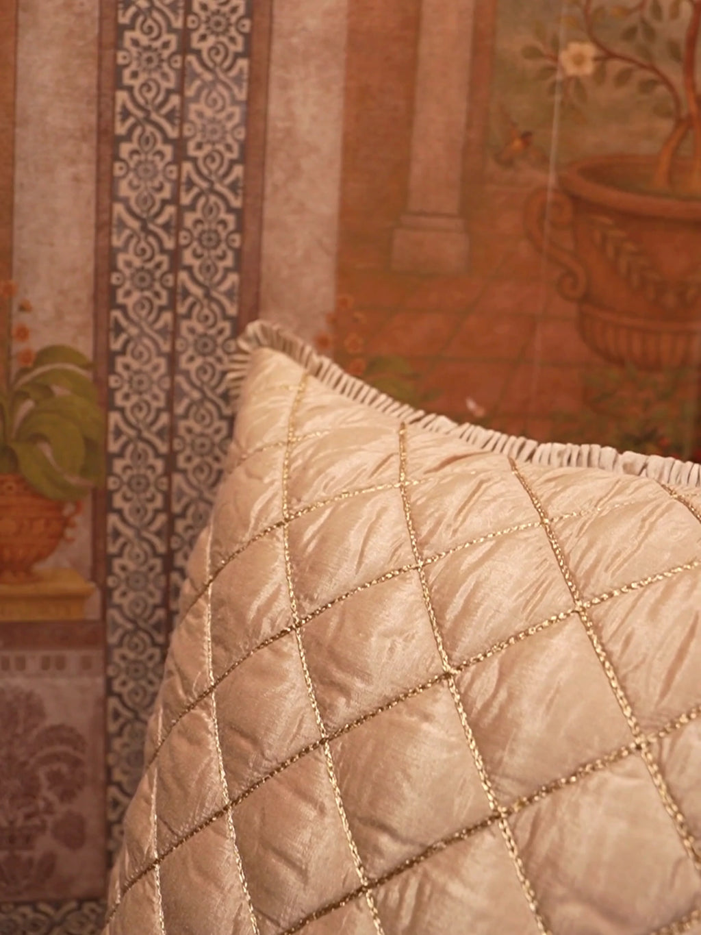 Rukhsar quilted silk cushion cover in gold with diamond quilting and a ruffled edge, shown up close against a painted wall