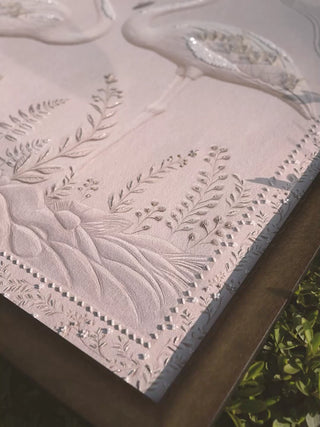 Sculpted Song embroidered wall art in white relief: a flamingo, ferns and sequins raised on a pale ground, filmed at an angle outdoors