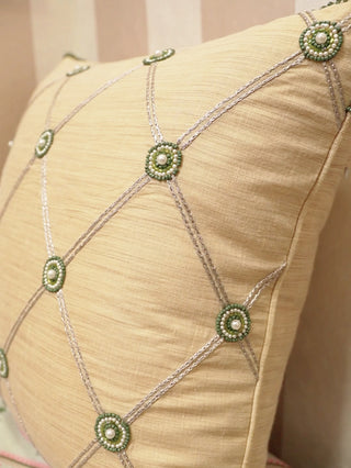 Shahzar cushion cover in beige with a silver lattice and green beaded medallions set with pearls, shown up close and on a daybed