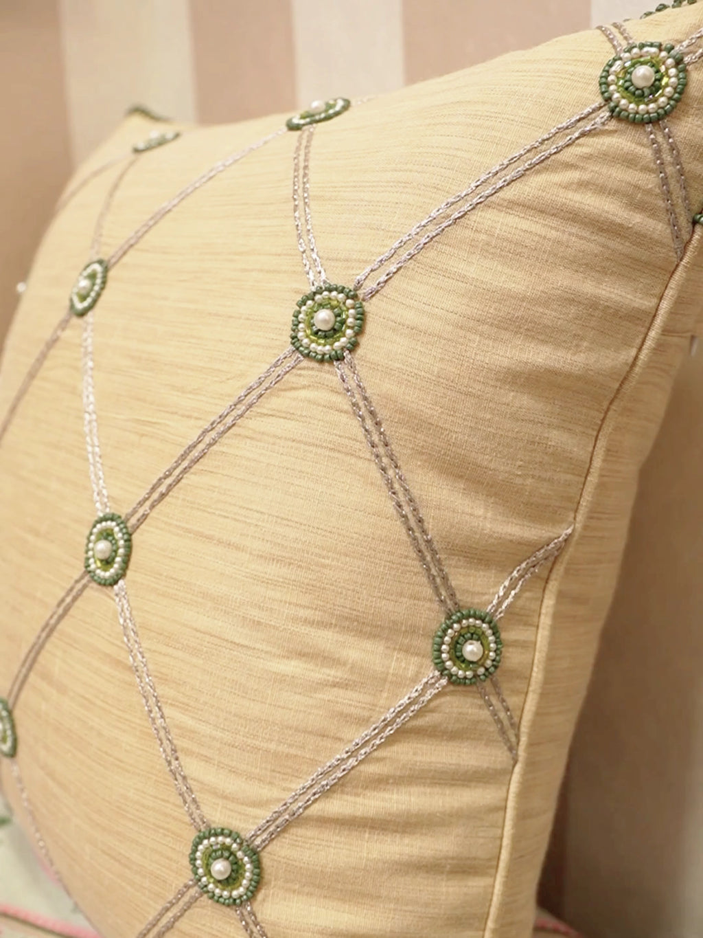 Shahzar cushion cover in beige with a silver lattice and green beaded medallions set with pearls, shown up close and on a daybed