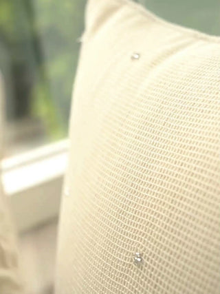 Stardust cushion cover in ivory open-weave linen with scattered tiny beads, up close and on a window seat beside white flowers