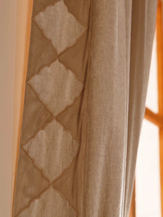 Storah readymade curtain in taupe linen with a stacked diamond border, shown up close and tied back at a window as a woman passes