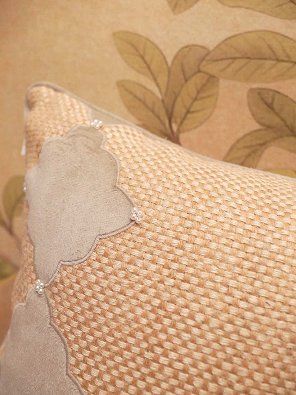 The Sirocco cushion cover in chunky natural weave with taupe velvet lobed shapes and pearl clusters, shown up close on a sofa