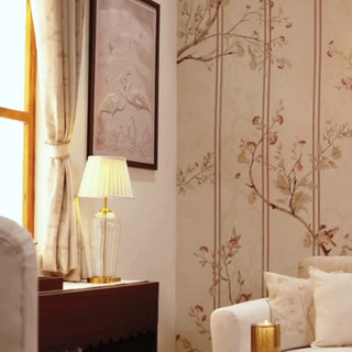The Syntax of Spring wallpaper with slim stripes and flowering branches in blush and taupe, shown behind a lamp, brass sconces and framed art