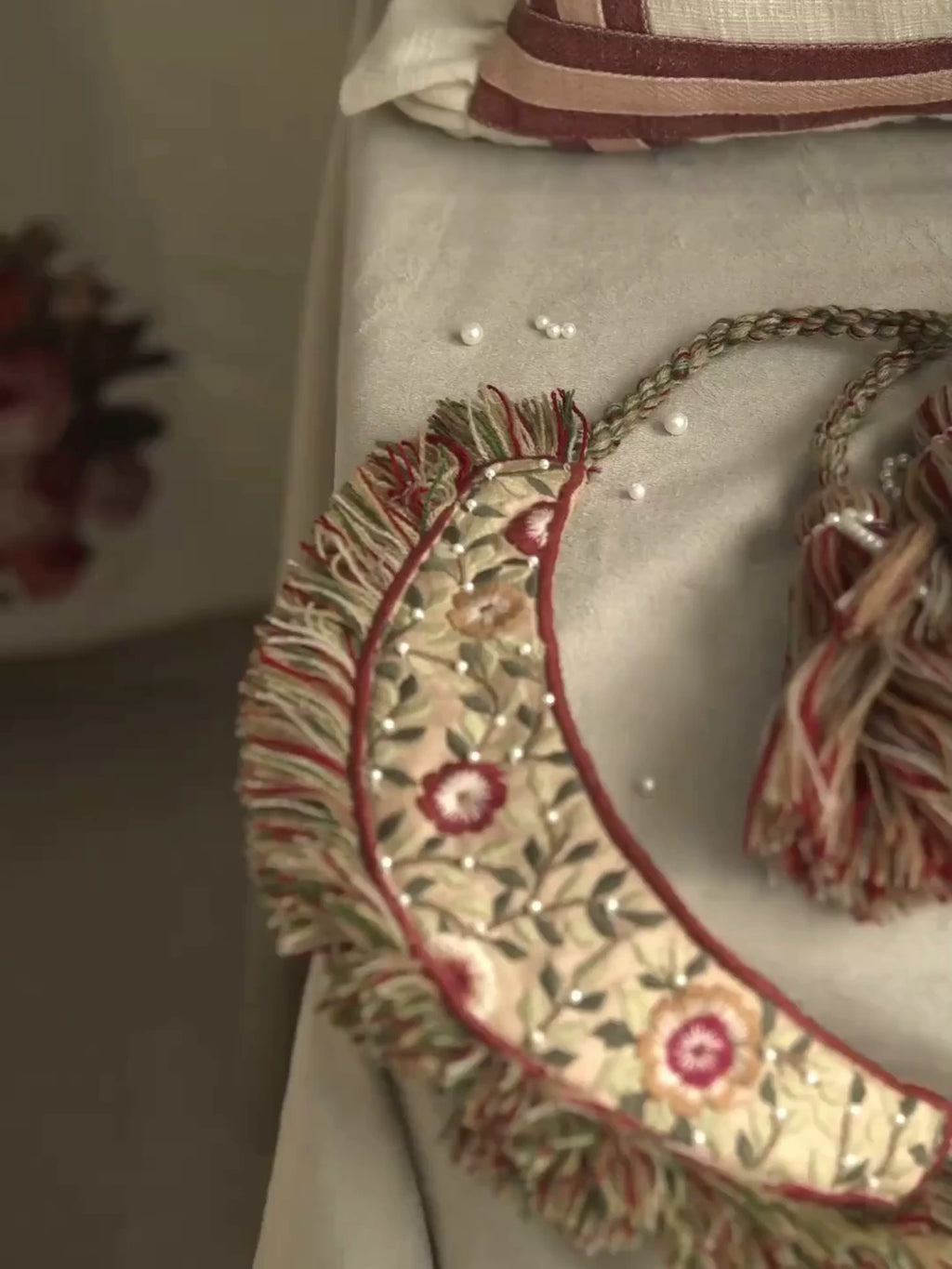 Close view of the Thiya curtain tieback: a crescent of crewel-embroidered florals with fringe and a striped tassel on a linen curtain