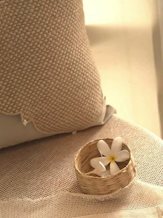 Zayan Weave cushion cover in taupe with a jute quatrefoil panel, pearl clusters and corded piping, beside a small basket of flowers