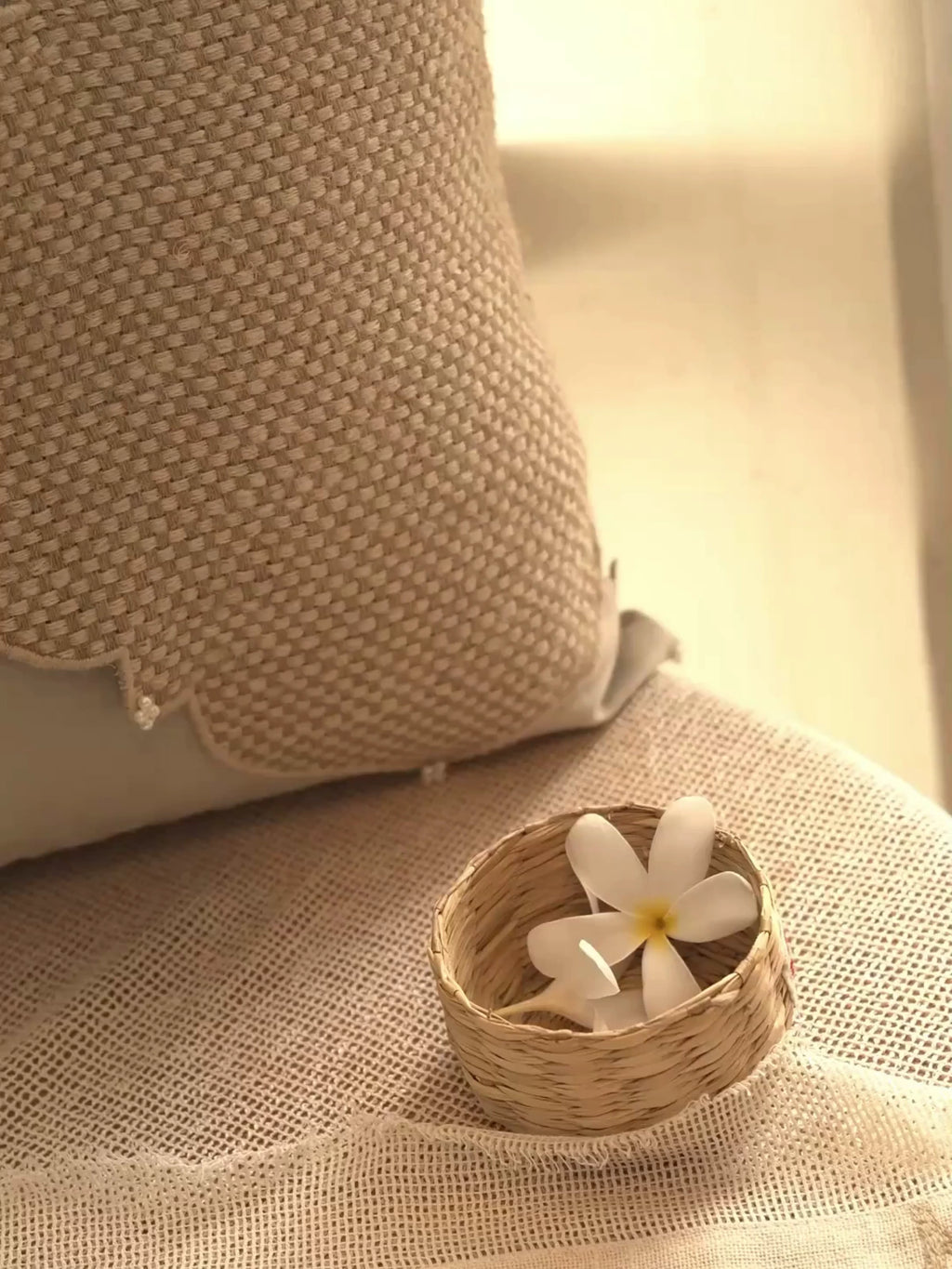 Zayan Weave cushion cover in taupe with a jute quatrefoil panel, pearl clusters and corded piping, beside a small basket of flowers