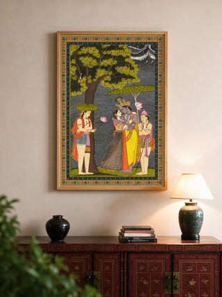 The Radha Krishna wall art in a wood frame, displayed above a red patterned console with books and a ceramic lamp.