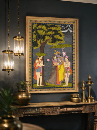 The Radha Krishna wall art in a wood frame, displayed on a dark charcoal wall above a carved wooden console with brass pieces.