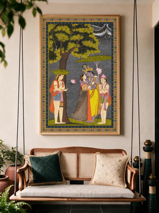 The Radha Krishna wall art in a wood frame, hung above a wooden hanging swing styled with cushions and potted plants.