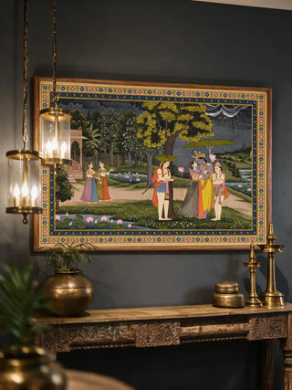 The Radha Krishna wall art framed and installed above a carved wood console table beside hanging brass lanterns in an entryway view-foyer