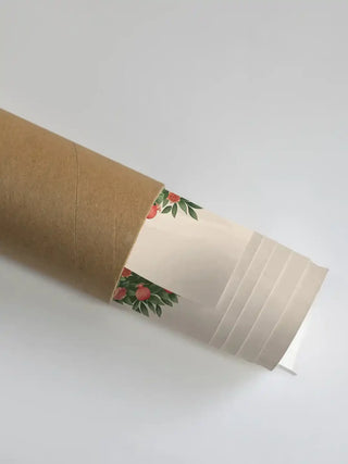 The Rajasi Van wall art partially unrolled from its kraft paper shipping tube, showing a sprig of red pomegranates and leaves on a cream ground.