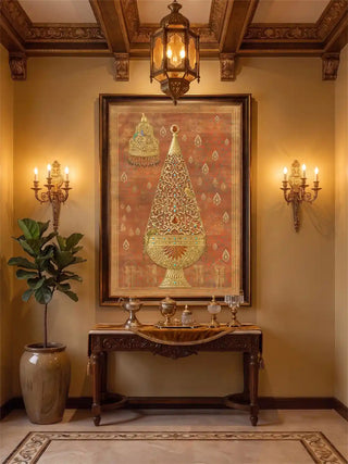 Rajghrana wall art in rust and gold, framed in dark wood between brass candle sconces above a carved console with silver vessels and a fiddle leaf fig in a foyer with a coffered ceiling.