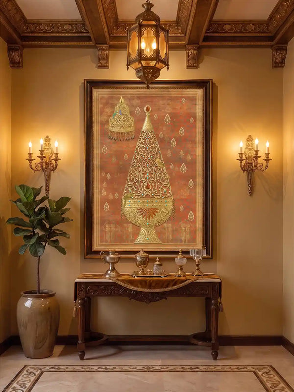 Rajghrana wall art in rust and gold, framed in dark wood between brass candle sconces above a carved console with silver vessels and a fiddle leaf fig in a foyer with a coffered ceiling.