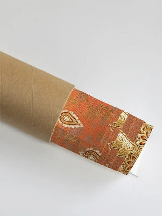 Rajghrana wall art print in rust and gold rolled in a kraft shipping tube, showing the paisley motifs and gilded filigree edge.