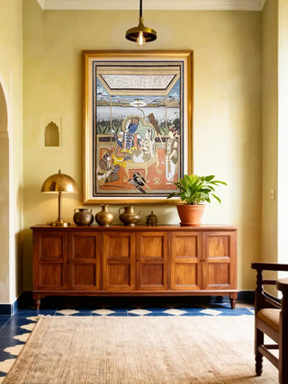Gold framed Ram Darbar wall art displayed above a wooden console table in a warm yellow foyer