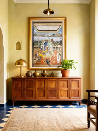 Gold framed Ram Darbar wall art displayed above a wooden console table in a warm yellow foyer