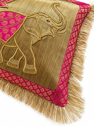 Close-up of the Rangrez cushion: a gold-outlined elephant with a pink brocade saddle cloth on a gold ground, framed by pink brocade and fringe.