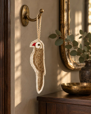 Ranjha ivory and gold embroidered bird charm hanging from an antique brass wall hook.