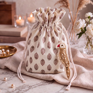 The Ranjha Parrot Hanging Charm in Ivory & Gold styled beside a cream potli bag block-printed with a repeating leaf motif.