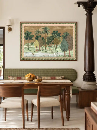 The Ranthambore forest landscape wall art in a dark wood frame, displayed above a green banquette in a dining nook with brass bowls on the table.