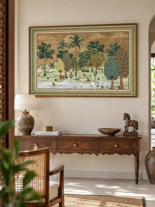 The Ranthambore forest landscape wall art in a wood frame, displayed above a wooden console with a lamp, books and a carved horse figurine.
