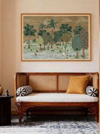 Framed Ranthambore Forest wall art in forest green above a rattan cane daybed with ochre and striped cushions in a warm living room.